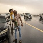 A man holds his child as people stand in the rain during a "rain chase" in the emirate of Sharjah on Saturday. The UAE experiences so little rainfall that “chasing” rain has become a niche hobby for some residents, who have taken to following Muhammed Sajjad, known as "The Weatherman,” as he finds the best places to enjoy the rare occasion of wet weather. (Fadel Senna/AFP via Getty Images)